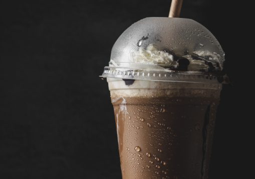 A vertical closeup of a plastic cup of cold coffee with a vanilla cream.